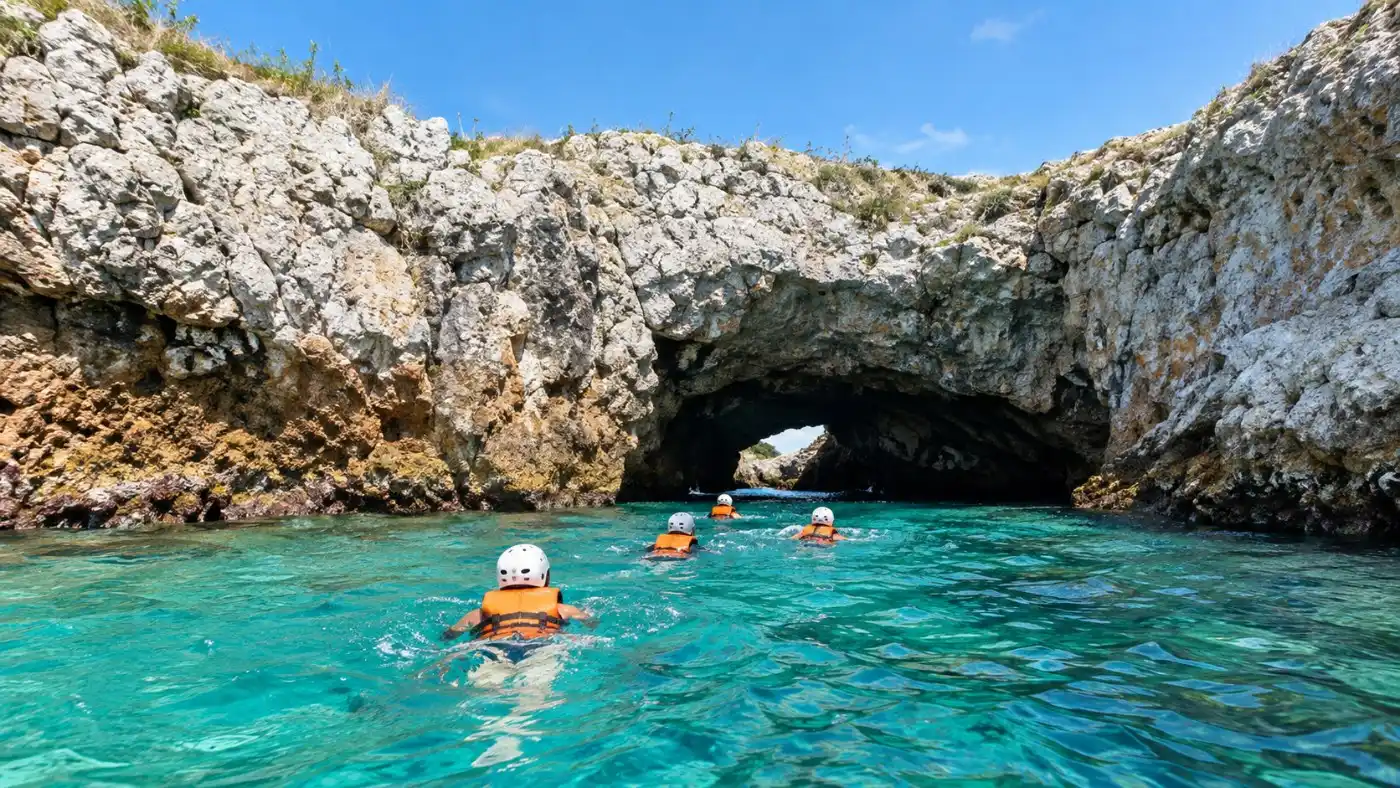Schwimmer in Schwimmwesten und Helmen schwimmen durch einen dunklen Felsentunnel aus türkisfarbenem Wasser